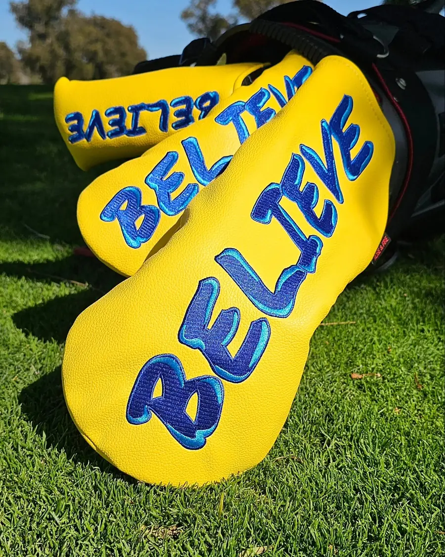 Three Believe covers resting against a golf bag on the course
